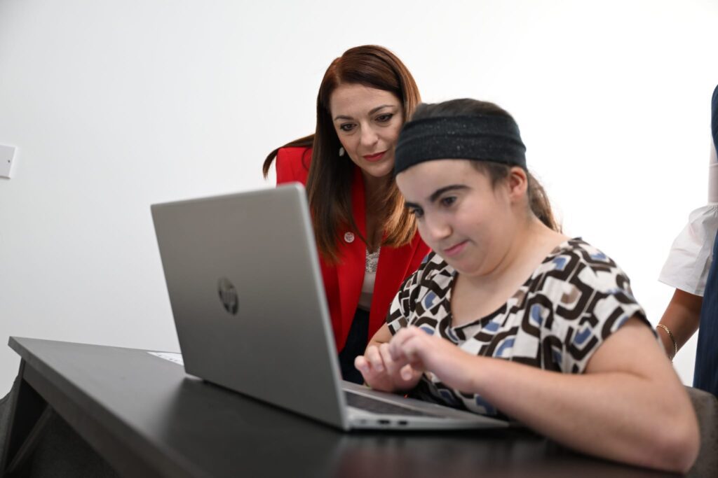 Il-Ministru Julia Farrugia ħdejn persuna b'diżabilità tfittex impjieg mill-laptop.