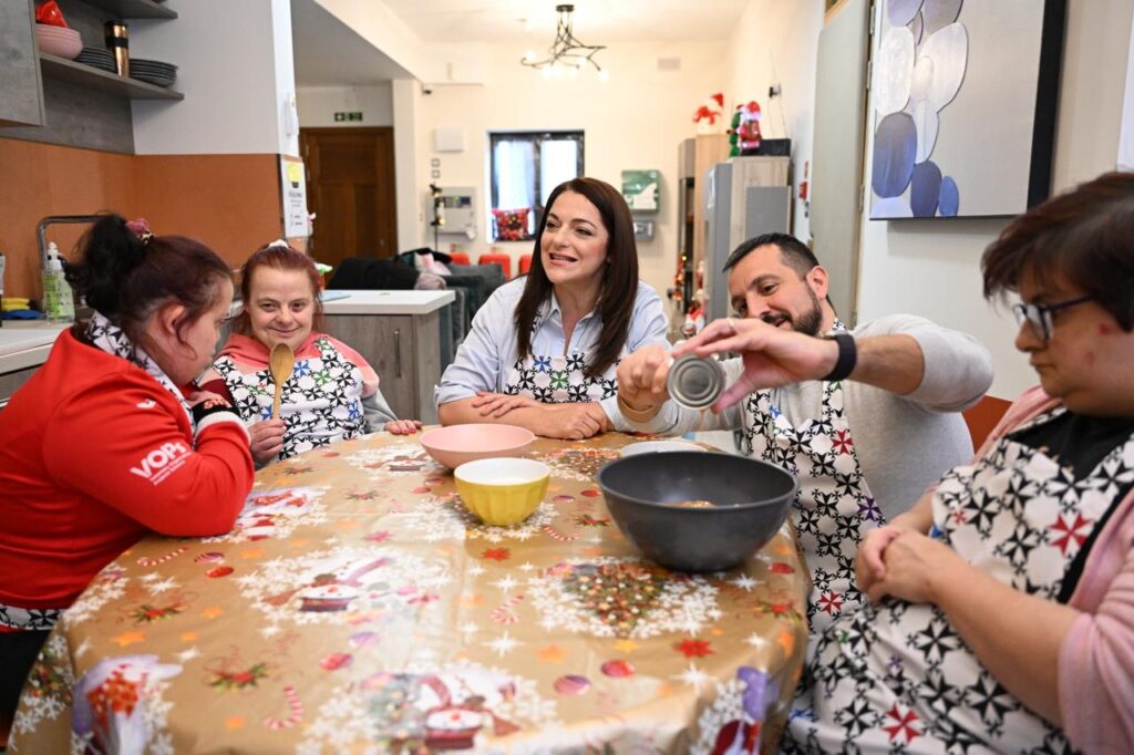 Il-Ministru Julia Farrugia u l-Kap Eżekuttiv Oliver Scicluna bilqeda mal-mejda kil-kċina ma' tlett persuni b'diżabilità, jagħmlu deżerta
