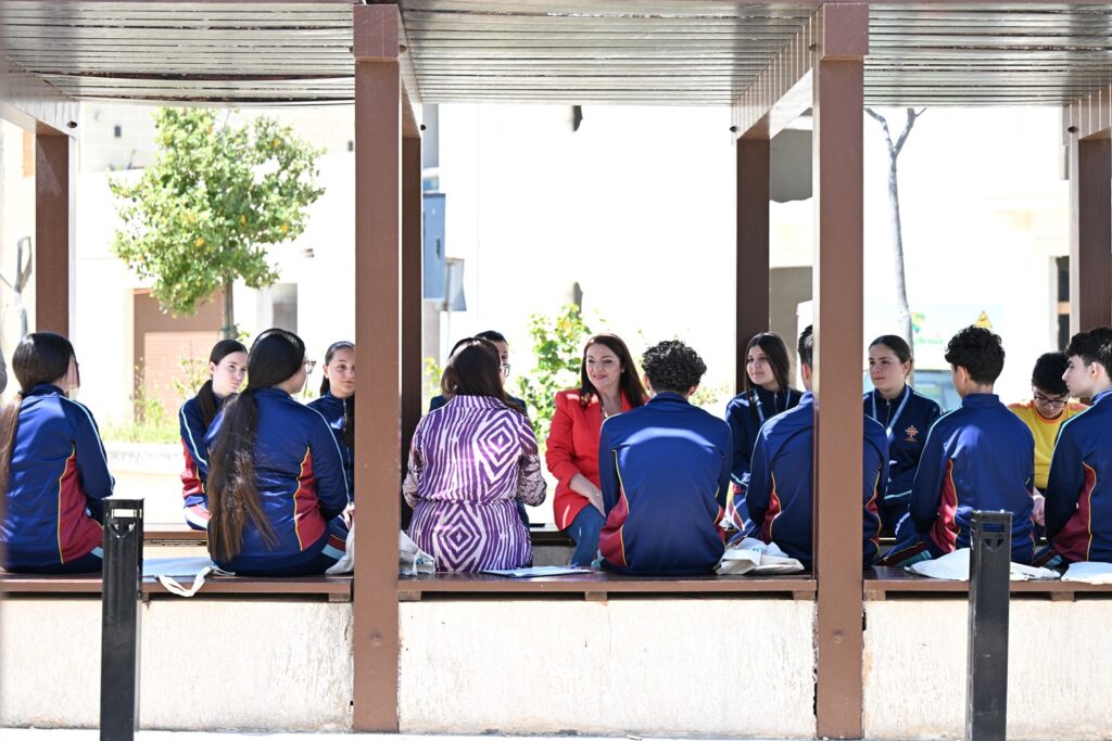 Il-Ministru Julia Farrugia ma' numru ta' studenti bilqiegħda fuq żewġ bankijiet faċċata ta' xulxin