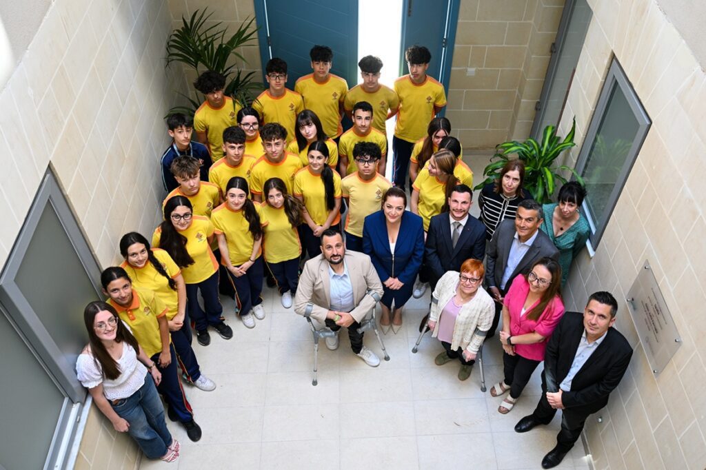 Ritratt ta' Julia Farrugia, Oliver Scicluna, studenti mill-Kulleġġ San Benedittu Ħal Kirkop, fost nies oħrajn, jitbissmu għar-ritratt ġewwa l-binja
